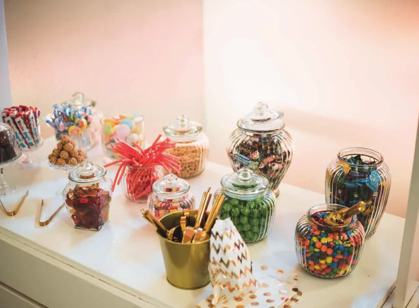 Candybar mit Süßigkeitengläsern und goldenen Zangen auf weißer Kommode