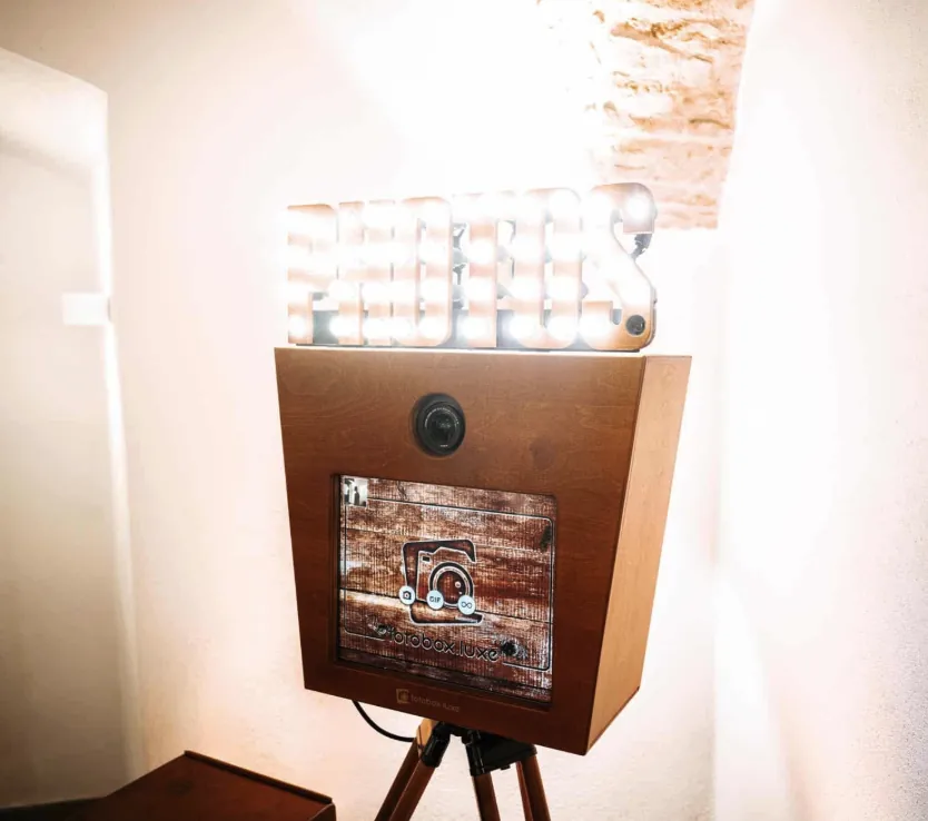 Hölzerne Fotobox mit leuchtendem Photos-Schriftzug unter einem Gewölbe
